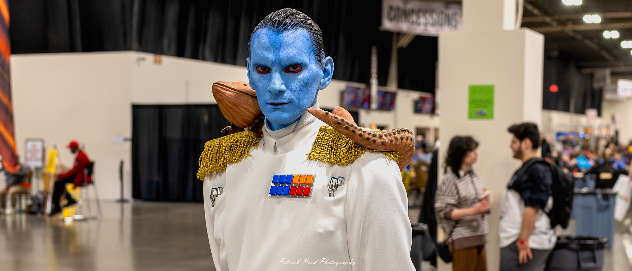 "Cosplayer dressed as Grand Admiral Thrawn from Star Wars, featuring the character's signature white military uniform, high-ranking officer's insignia, blue skin, red eyes, and distinct facial features, capturing the strategic and imposing presence of the Chiss tactician."